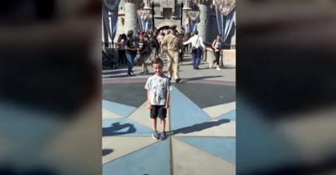 Kleiner Junge posiert in Disneyland für ein Foto, während sich sein Vater in seiner Marine Uniform durch die Menge anschleicht